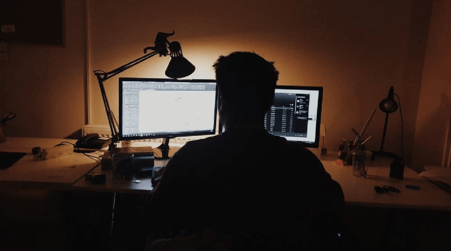 Person working at a dual-monitor desk setup at night